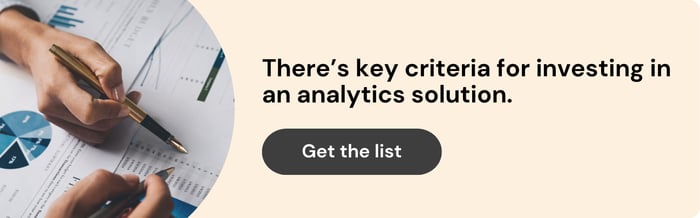 ID: On the left is a zoomed in image of two hands using fountain pens to point at a data points on a set of printed charts and graphs. On the right text reads: "there's key criteria for investing in an analytics solution. Get the list."